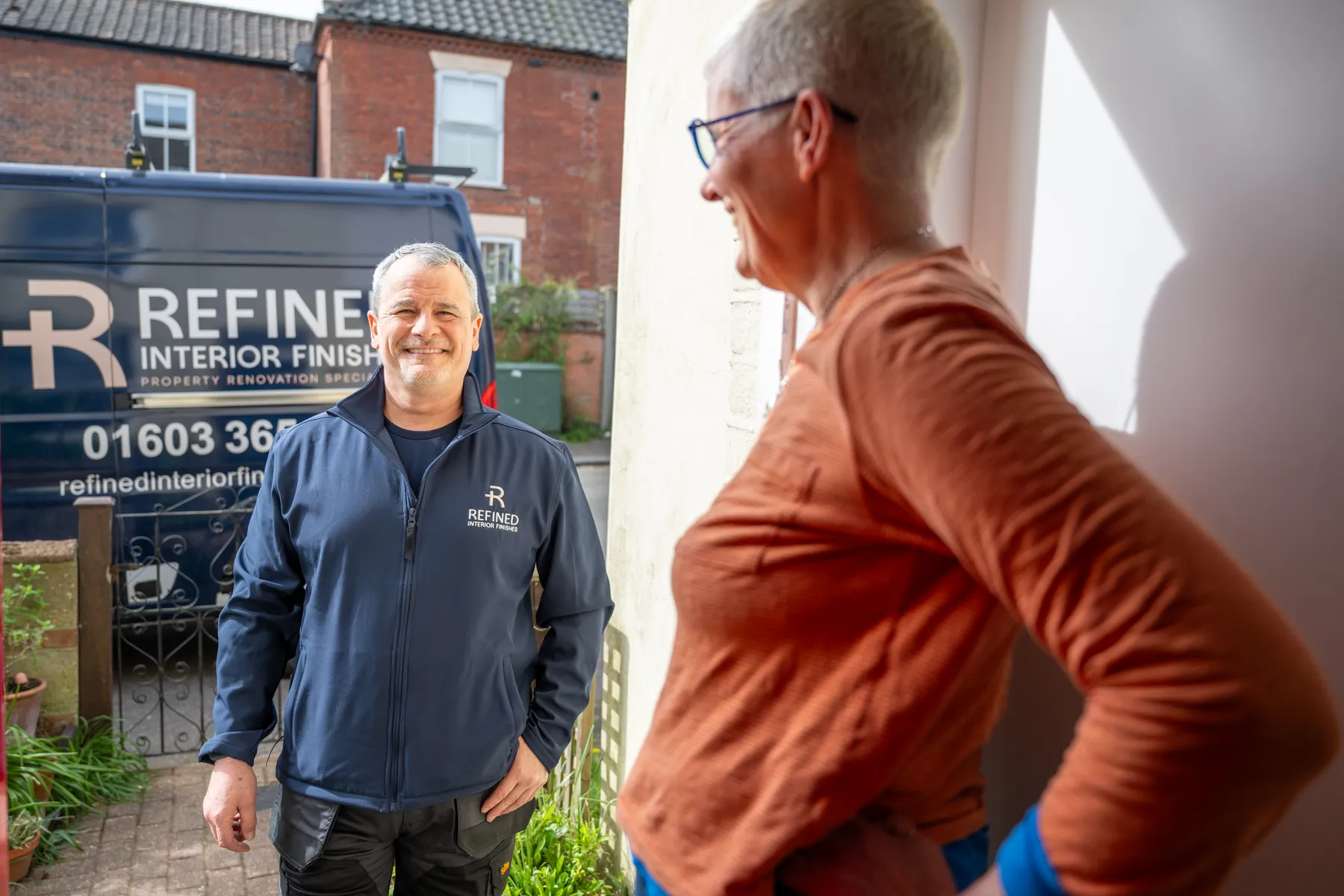 Kevin Smith of Refined Interior Finishes talking with a homeowner at their front door, with the company van parked behind