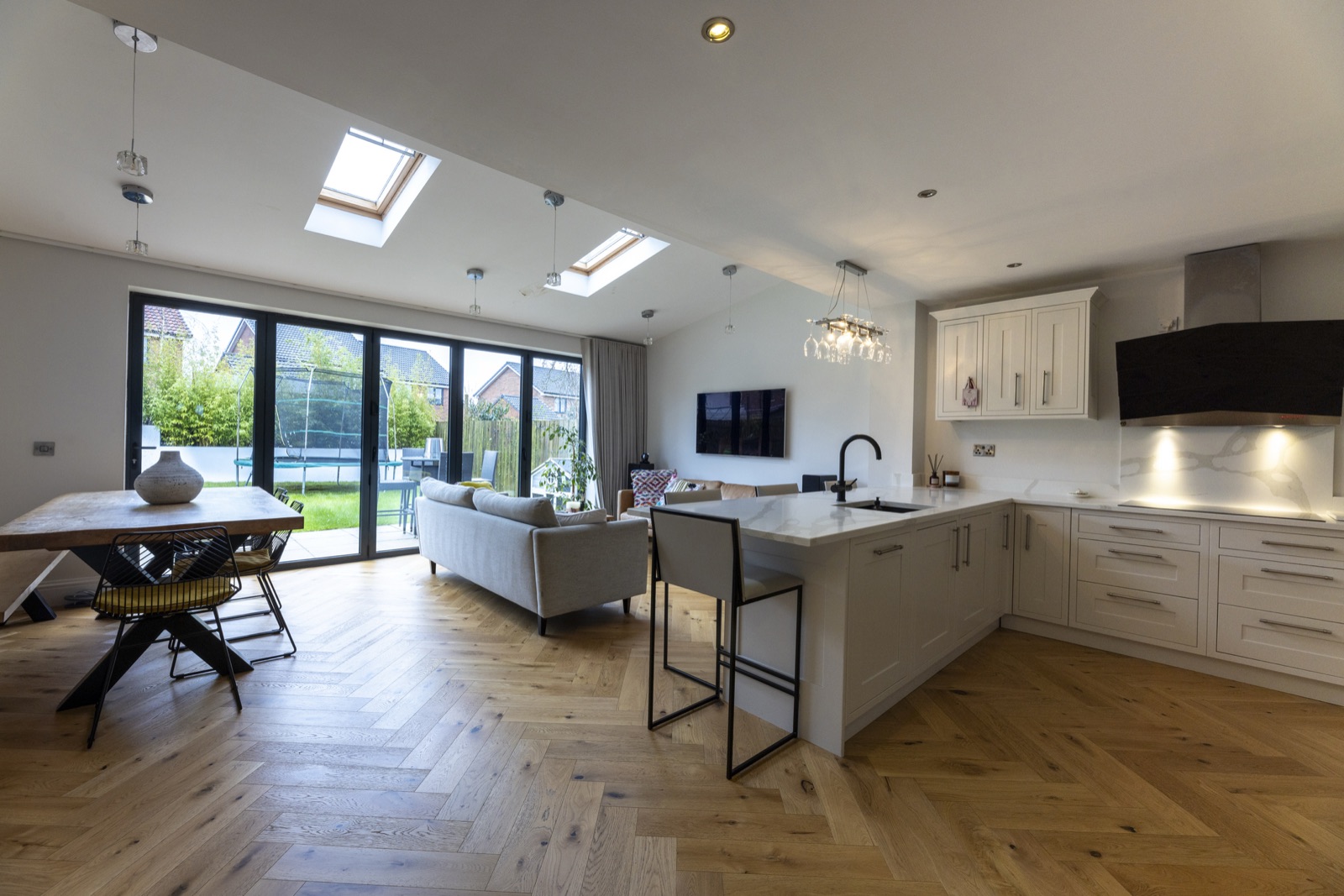 Open-plan kitchen and living space with herringbone wood flooring and bifold doors to the garden