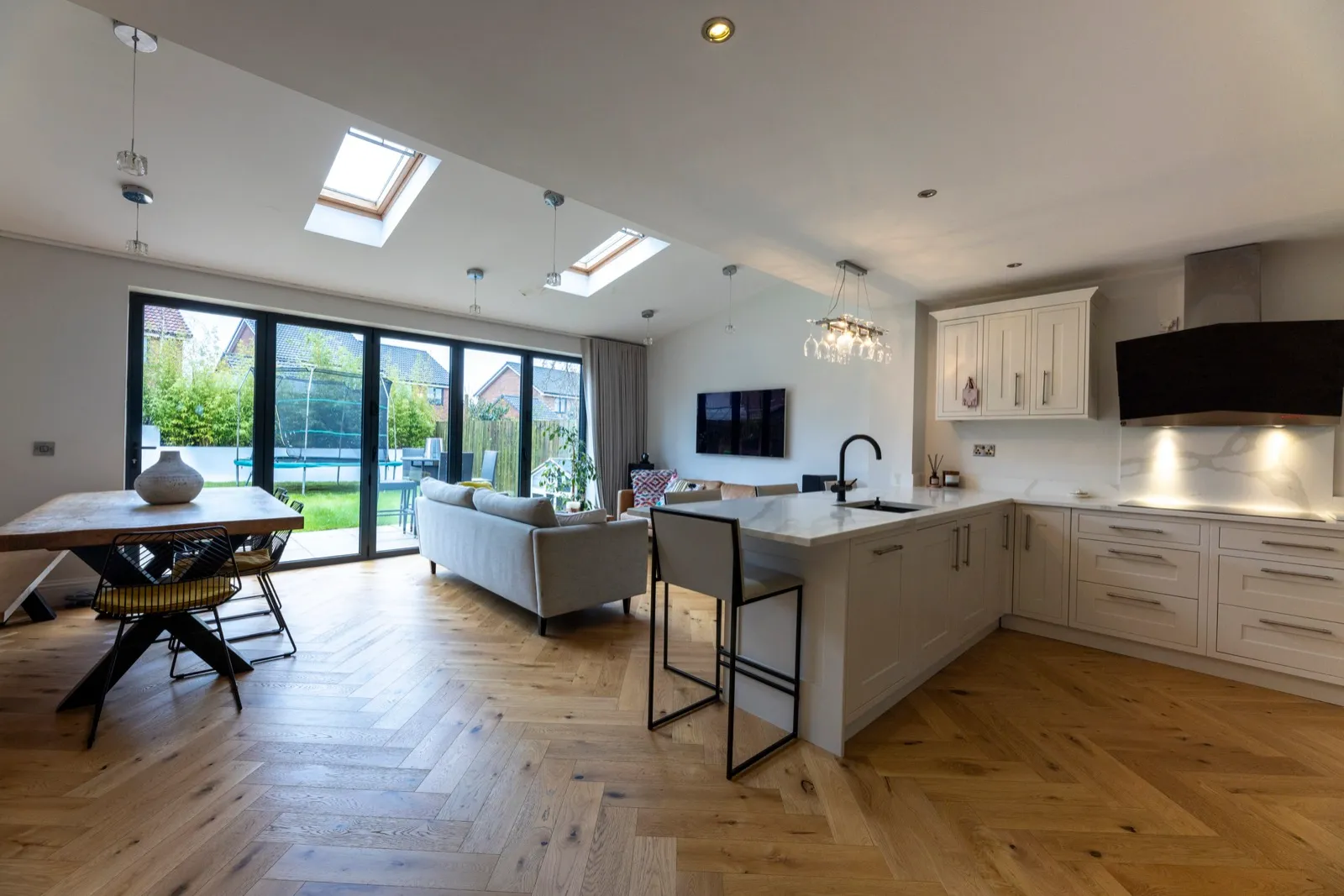 Open-plan kitchen and living space with herringbone wood flooring and bifold doors to the garden